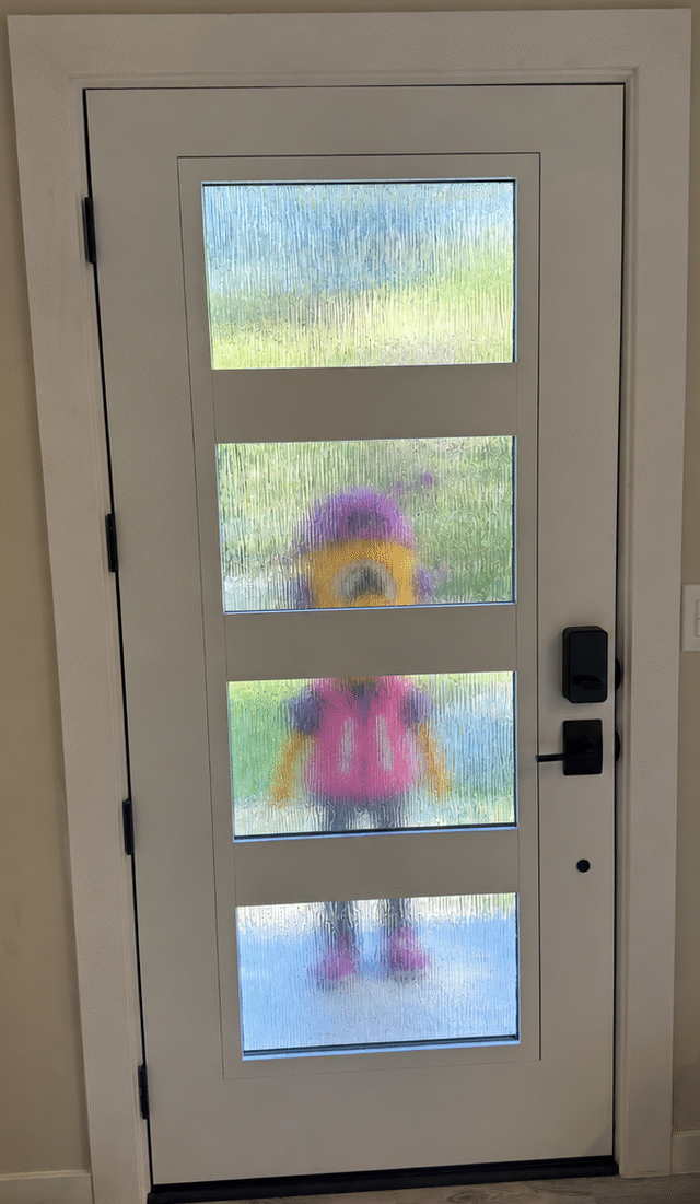 A small figure in a Minion costume standing outside a frosted glass front door, waiting to be let in